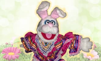 A stuffed bunny dressed in a colorful outfit is standing in the grass.