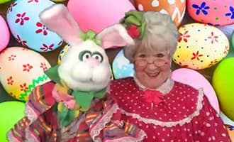 A woman dressed as an easter bunny in front of a bunch of easter eggs.